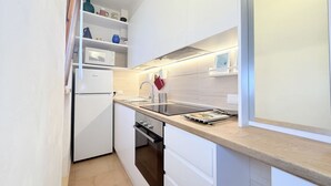 Une cuisine compacte avec des meubles blancs, un four encastré, un four à micro-ondes et un plan de travail en bois.
