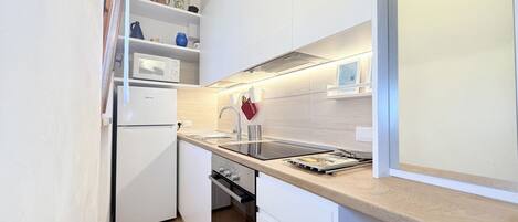 Una cocina compacta con armarios blancos, horno empotrado, microondas y encimera de madera.