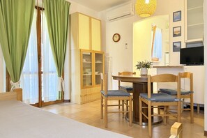 Ein Zimmer mit Esstisch, Stühlen, einem Schrank, einem Fernseher und einer Wanduhr.