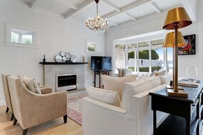 Ein modernes Wohnzimmer mit Kamin, bequemen Sitzgelegenheiten, einer Kristallleuchtre und einem großen Fenster mit Blick.