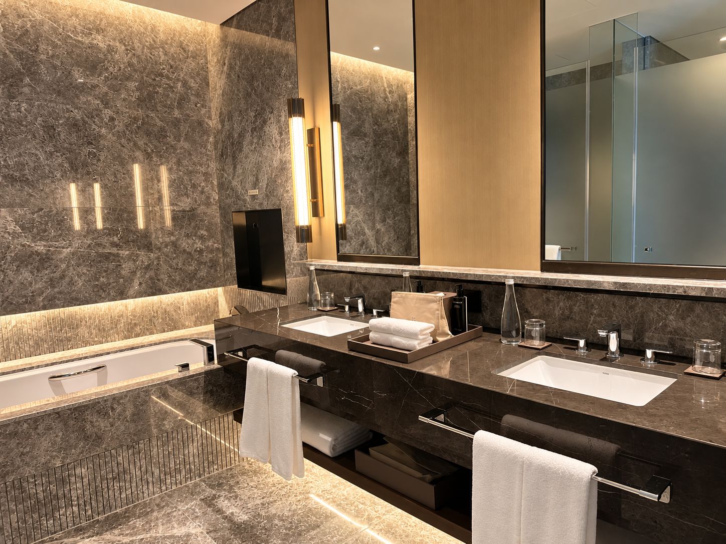 A modern bathroom with two sinks, a large mirror, and a bathtub.