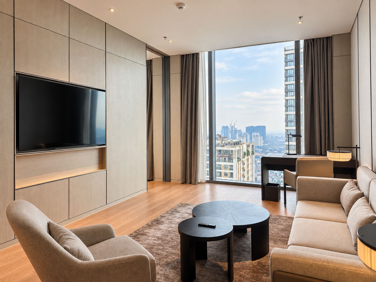 Una sala de estar moderna con un televisor de pantalla plana, un sofá, una mesa de centro y vistas a un paisaje urbano a través de ventanas amplias.