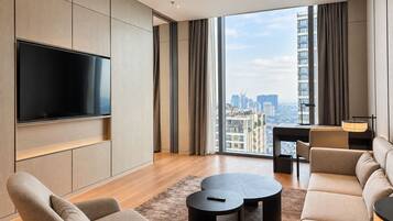 Una sala de estar moderna con un televisor de pantalla plana, un sofá, una mesa de centro y vistas a un paisaje urbano a través de ventanas amplias.
