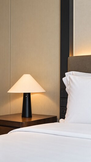 A hotel room with a bedside lamp, a bed with white bedding, and a headboard with a light panel. - Shilla Monogram Hanoi Westlake Hotel (Hanoi)