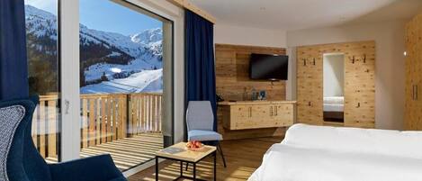 Une chambre d’hôtel moderne dotée d’une grande fenêtre, d’un téléviseur à écran plat, d’un bureau en bois, d’un canapé et d’un balcon offrant une vue sur des montagnes enneigées.