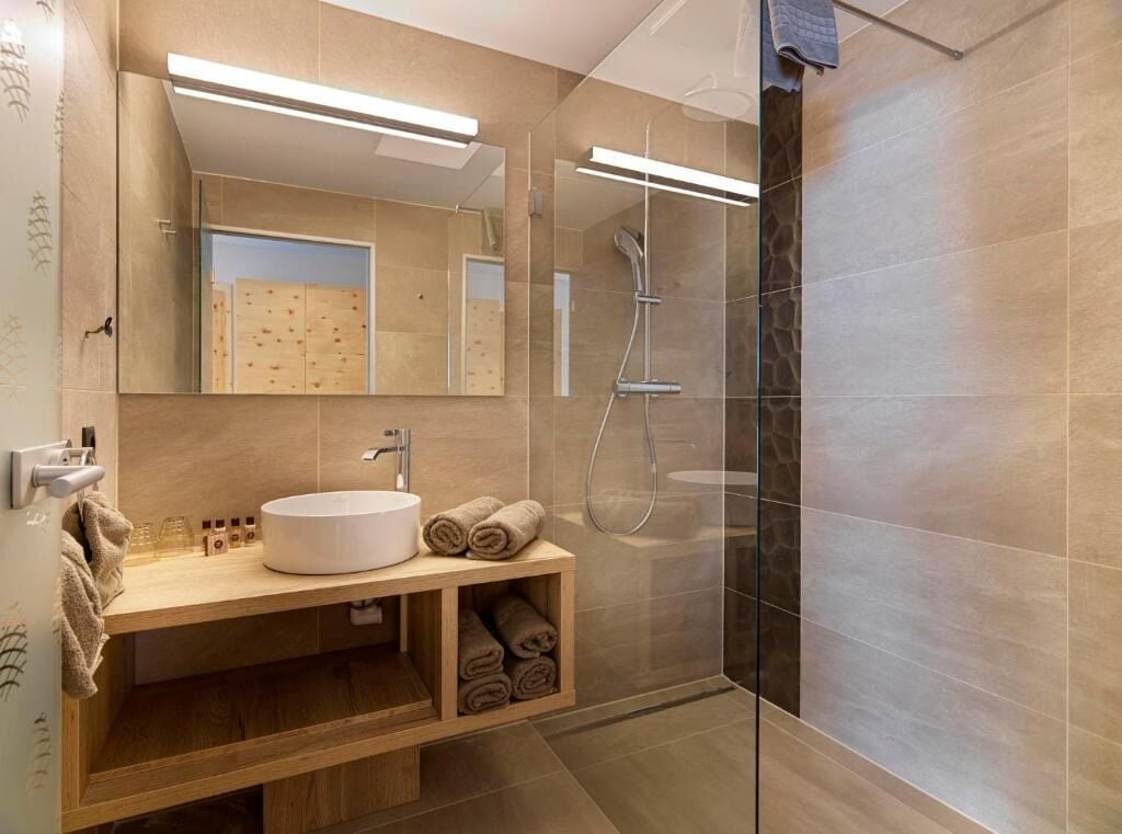 Une salle de bain moderne avec un grand miroir, un lavabo rond, une cabine de douche en verre et un meuble-lavabo en bois.