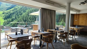 Een moderne hotelkamer met een balkon met uitzicht op een bebost dal, gemeubileerd met houten tafels en stoelen.