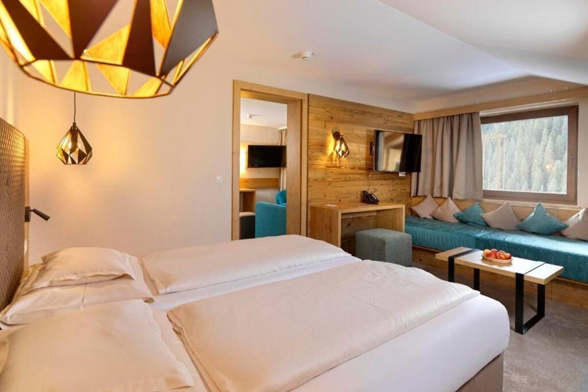 Una habitación de hotel con cama, sofá, televisor, escritorio y un amplio ventanal.