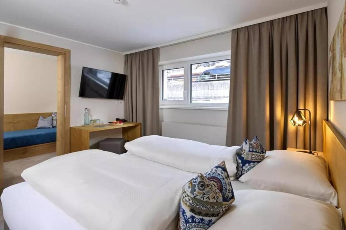 Habitación de hotel con cama, escritorio, televisor y ventana con cortinas.