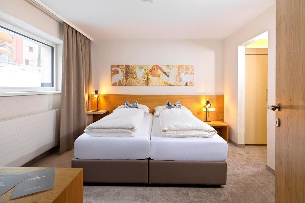Un lit double avec deux tables de chevet, une tête de lit, une fenêtre avec des rideaux, une œuvre d’art accrochée au mur et une porte.