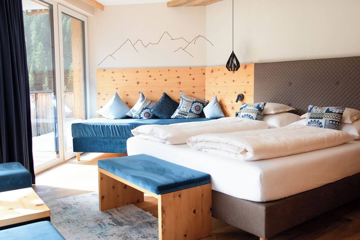 Un dormitorio moderno con una cama grande, dos camas más pequeñas, un banco y vistas al exterior.