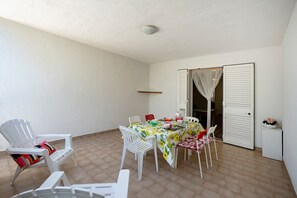 A small, enclosed patio area with a table set for dining, white chairs, a white tablecloth, and a white cabinet with a flower vase.