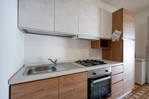 Una cocina con un lavamanos de acero inoxidable, estufa a gas, horno, armarios de madera y un refrigerador blanco.