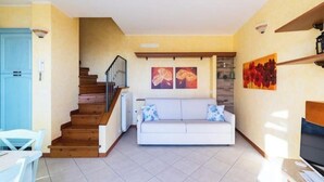 Een woonkamer met een trap, een witte bank en kunstwerken aan de muur.