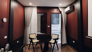 A room with a round table, two chairs, a window with curtains, an air conditioning unit, and a door. - Bee Stay Apartment Huy Van (Hanoi)