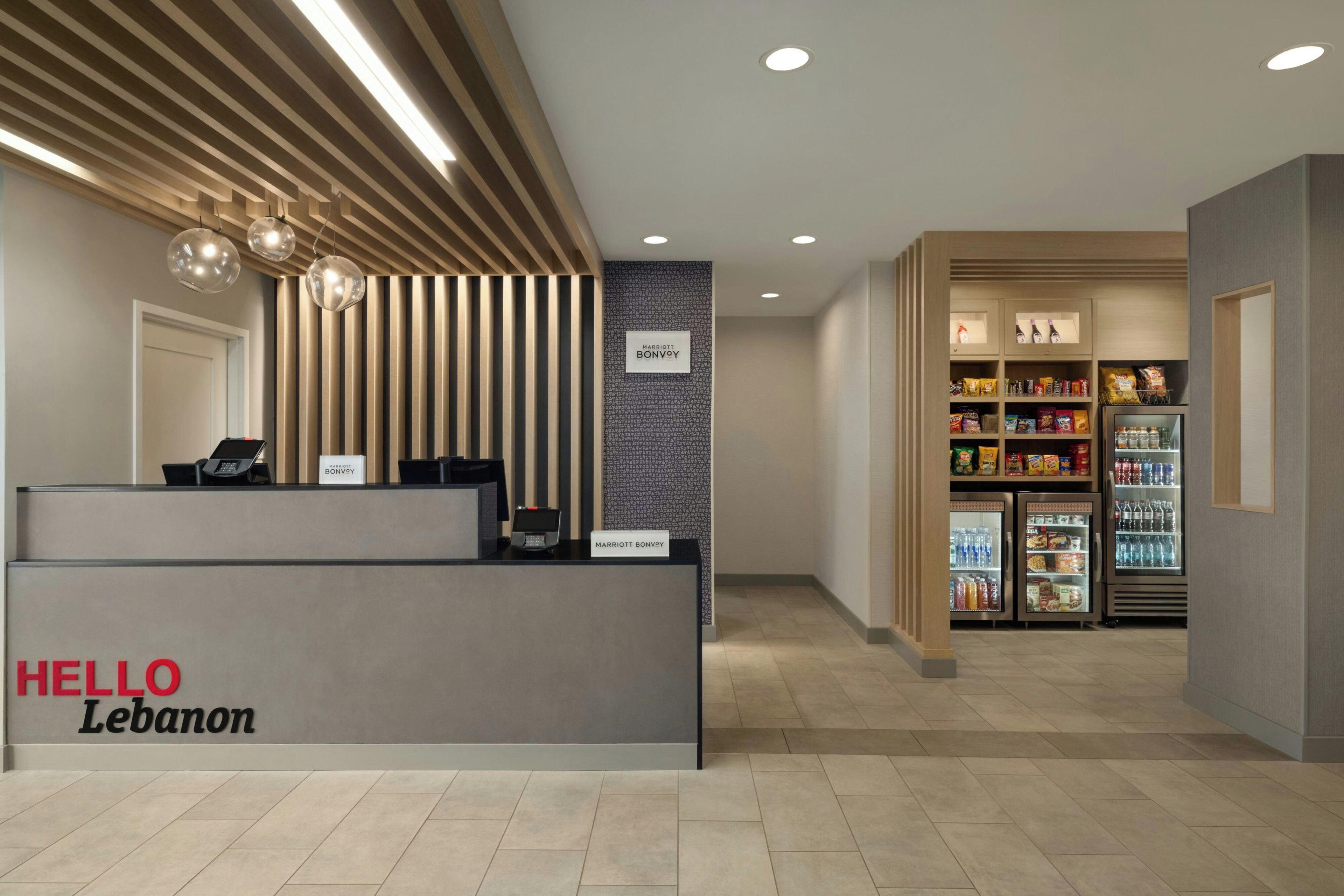 A hotel reception area with a modern design, including a reception desk, a wall-mounted sign, and a vending machine with snacks and beverages.
