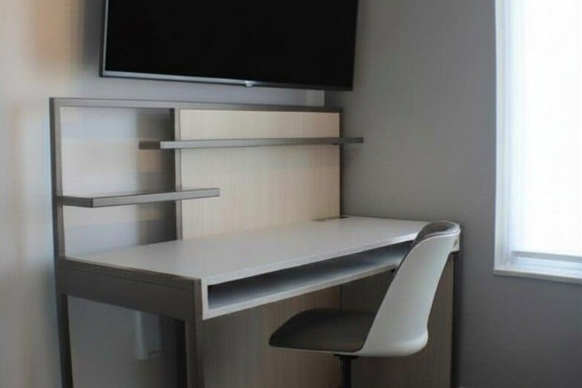 A modern office desk with a flat-screen TV, a chair, and a window with blinds.