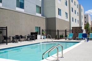 A swimming pool with a metal ladder, surrounded by lounge chairs and tables, with a building featuring a modern design in the background. - TownePlace Suites by Marriott Lebanon PA (Lebanon)