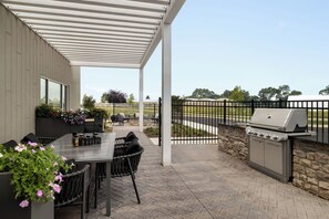 An outdoor patio with a grill, dining table, chairs, and a covered seating area.