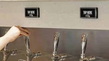 Uma estação de torneiras com várias opções e uma mão segurando um copo de cerveja.