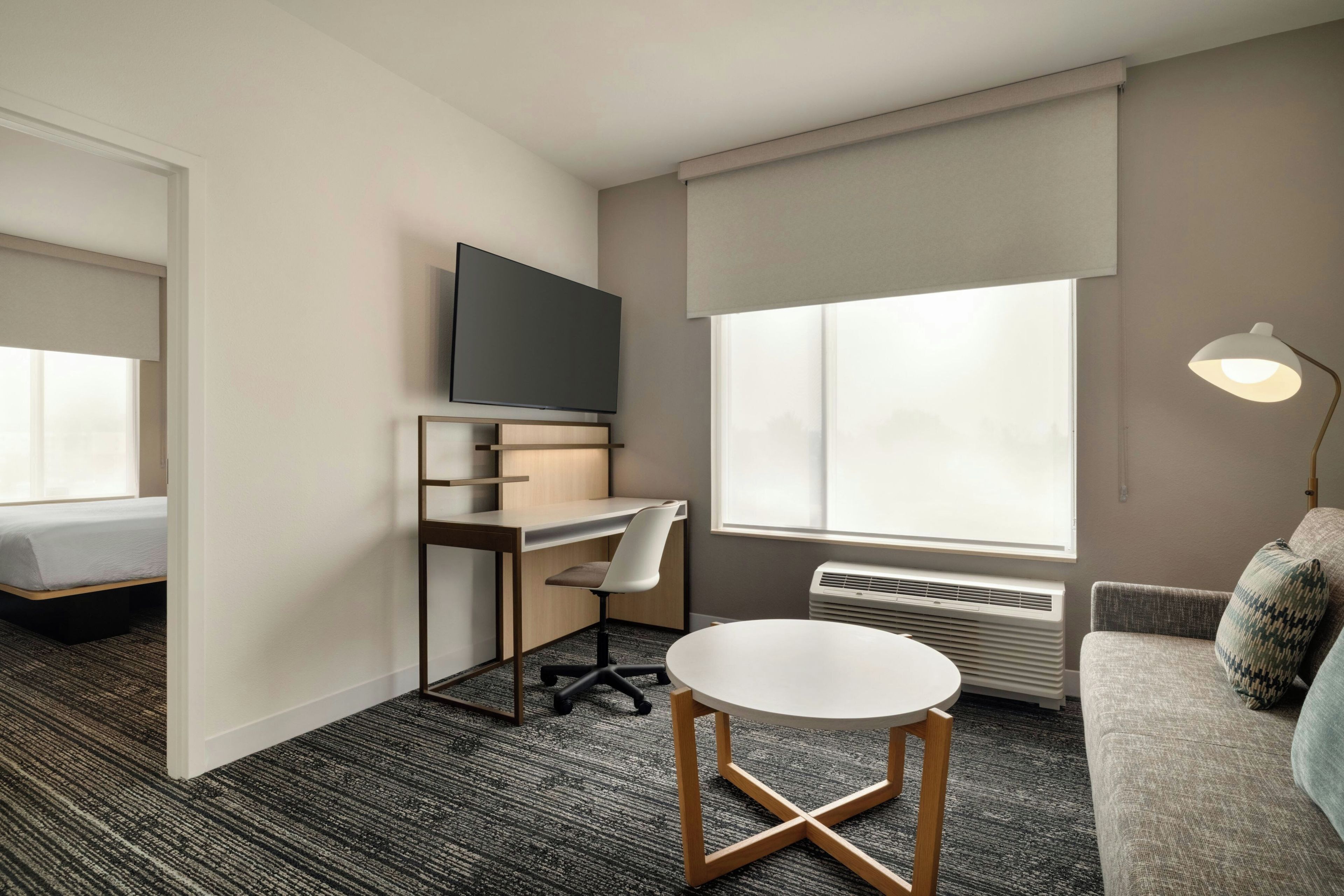Una habitación de hotel con una cama, un escritorio con silla, un televisor, una lámpara de pie y un sofá.