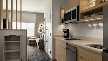 A modern kitchen with a built-in microwave, coffee maker, and a sink. There is a dining area with a table and chairs, and a sofa.
