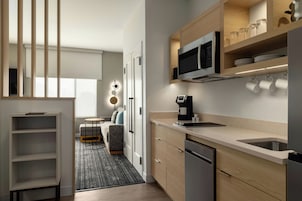 Una cocina moderna con microondas integrado, cafetera y un lavabo. Hay una zona de comedor con mesa y sillas, y un sofá.
