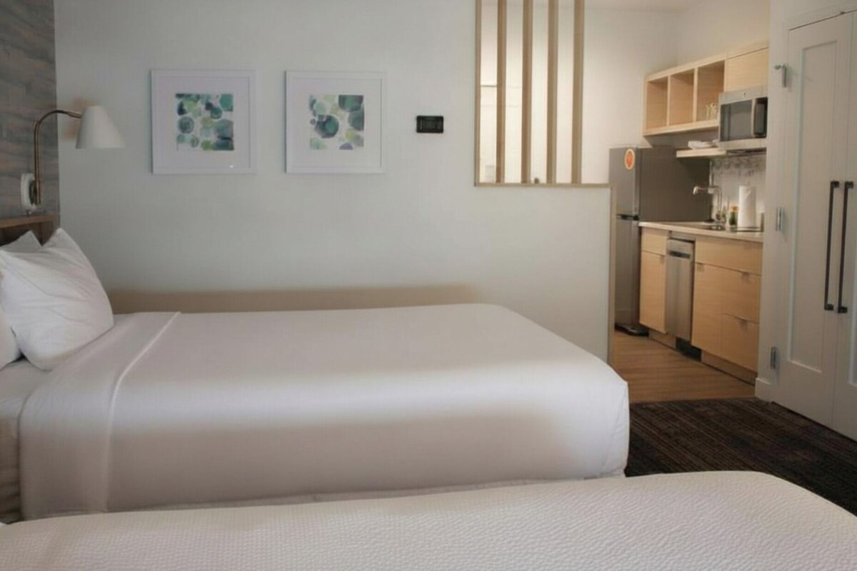 A hotel room with two beds, a kitchenette, and artwork on the wall.