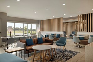 A modern hotel lobby with a sofa, chairs, tables, and a view of the outdoors. - TownePlace Suites by Marriott Lebanon PA (Lebanon)