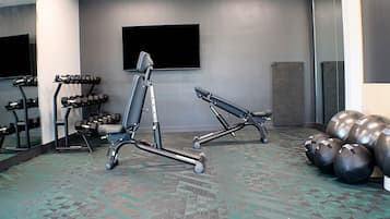 Un gimnasio con equipo de ejercicio, un espejo grande y un televisor en la pared.