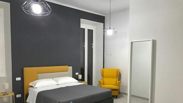 A modern bedroom with a bed, a chair, a mirror, and a pendant light. - Superior Room for 1 to 4 people   Piazza Bologna (Roma)