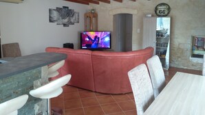 A living room with a red sofa, a television, and a dining area with a table and chairs. - Between river and town center - air-conditioned - 2 WCs - enclosed courtyard (Cognac)