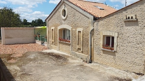 A stone building with a tiled roof, arched windows, and a small balcony with potted plants. - Between river and town center - air-conditioned - 2 WCs - enclosed courtyard (Cognac)