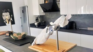 Una cucina moderna con un piano di lavoro nero, mobili bianchi, una rastrelliera pensile per pentole e un cesto decorativo in vimini.
