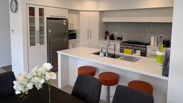 A modern kitchen with a central island, stainless steel appliances, and a dining area with bar stools. - Modern Napier Comfort (Napier)