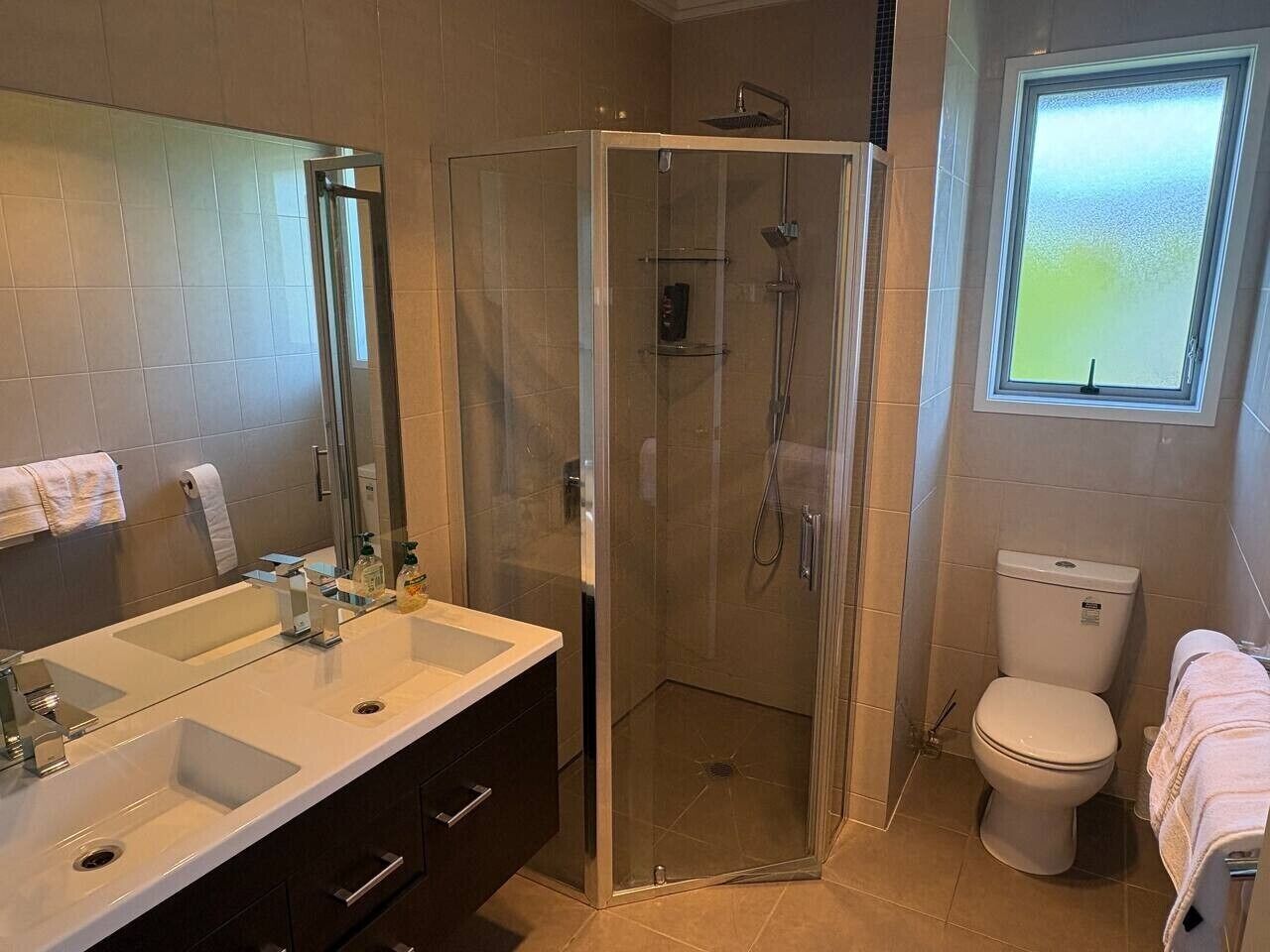 A bathroom with a glass-enclosed shower, a toilet, and a sink with a mirror.