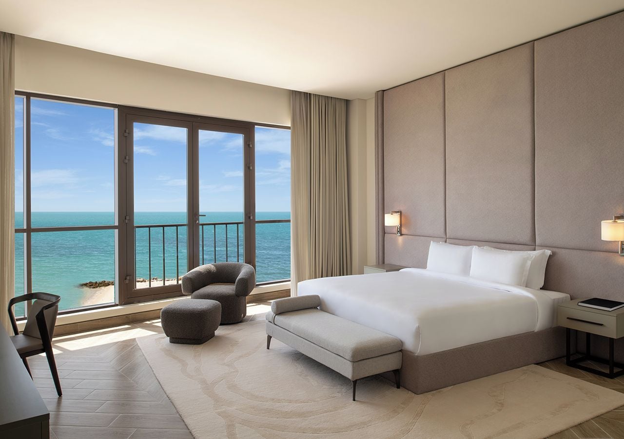 A hotel room with a large bed, a desk, a chair, a sofa, and a view of the ocean.