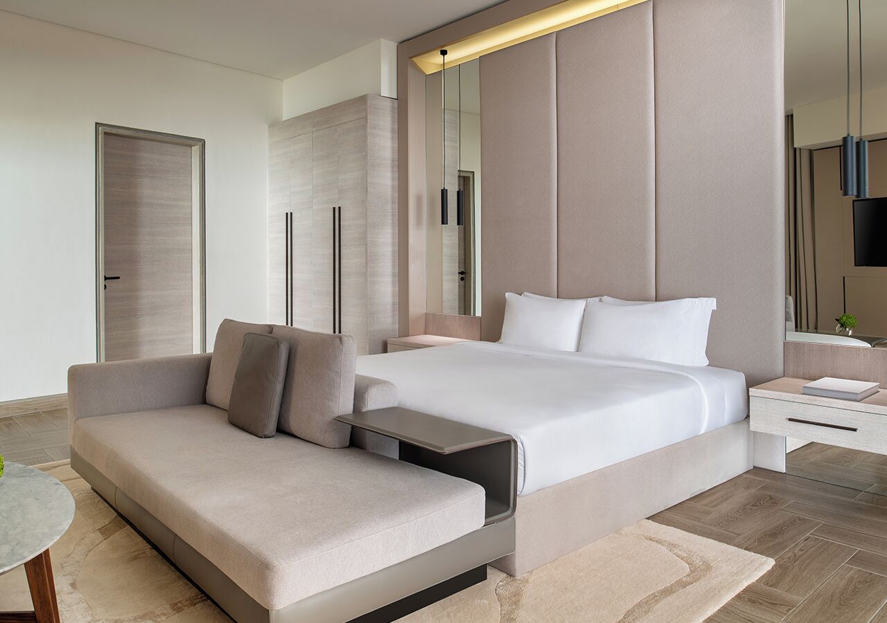 A modern hotel room with a bed, sofa, bedside table, and a mirror.