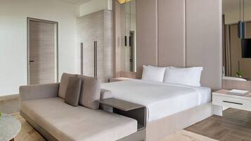 A modern hotel room with a bed, sofa, bedside table, and a mirror.