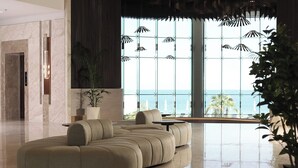 A modern living room with a large sectional sofa, a potted plant, and a view of the ocean through large windows. - Ray Hotel by Cloud 7 (Mangaf)