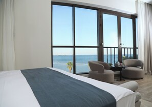 A hotel room with a large bed, two armchairs, a small table, and a balcony with a view of the sea.