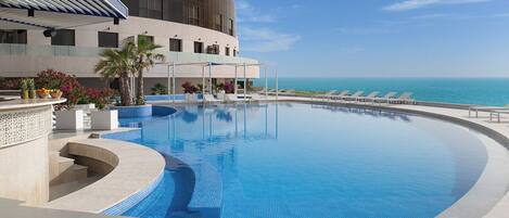 Una piscina al aire libre, sombrillas, sillones reclinables de piscina