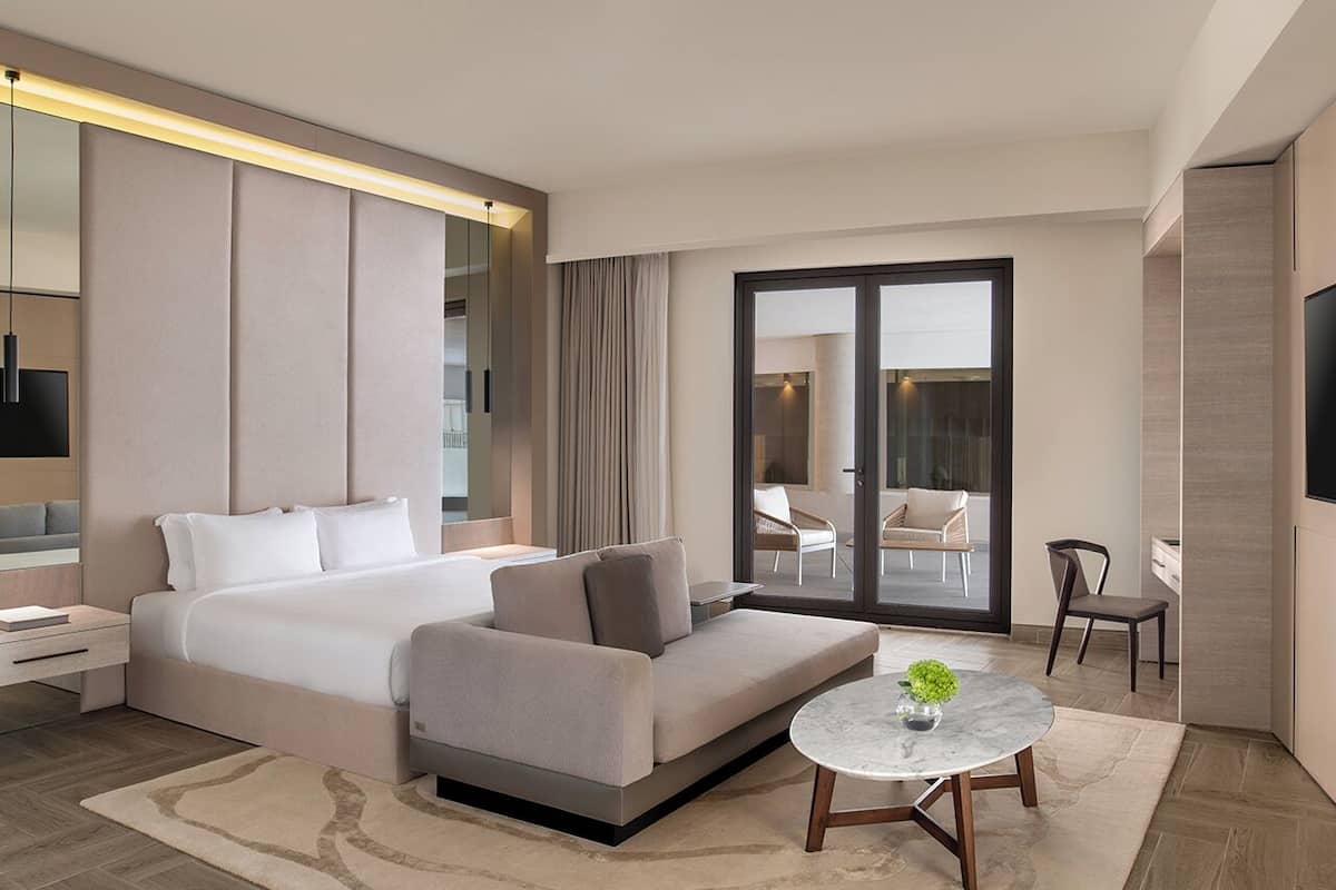Une chambre dâhĂŽtel moderne, Ă©quipĂ©e dâun lit, dâun canapĂ©, dâune table ronde et offrant une vue Ă travers une porte vitrĂ©e.