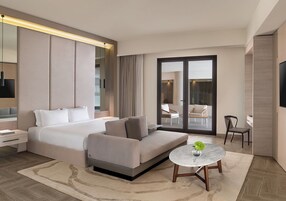 Habitación de hotel moderna con cama, sofá, mesa redonda y vistas a través de un ventanal.