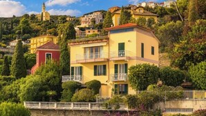 A hillside residential area with a yellow building featuring balconies and a red building in the foreground. - Hostdomus - Villa Gabriella (Alassio)