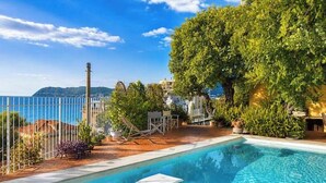 A swimming pool with a view of the sea, surrounded by greenery and a fence. - Hostdomus - Villa Gabriella (Alassio)