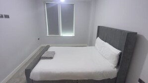 A small, neatly made bed with a grey headboard and white bedding in a room with light-colored walls and a single window. - 2 Bedroom - Rubix (London)