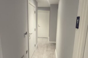 A narrow hallway with a door at the end, a light switch, and a wall-mounted light fixture. - 2 Bedroom - Rubix (London)