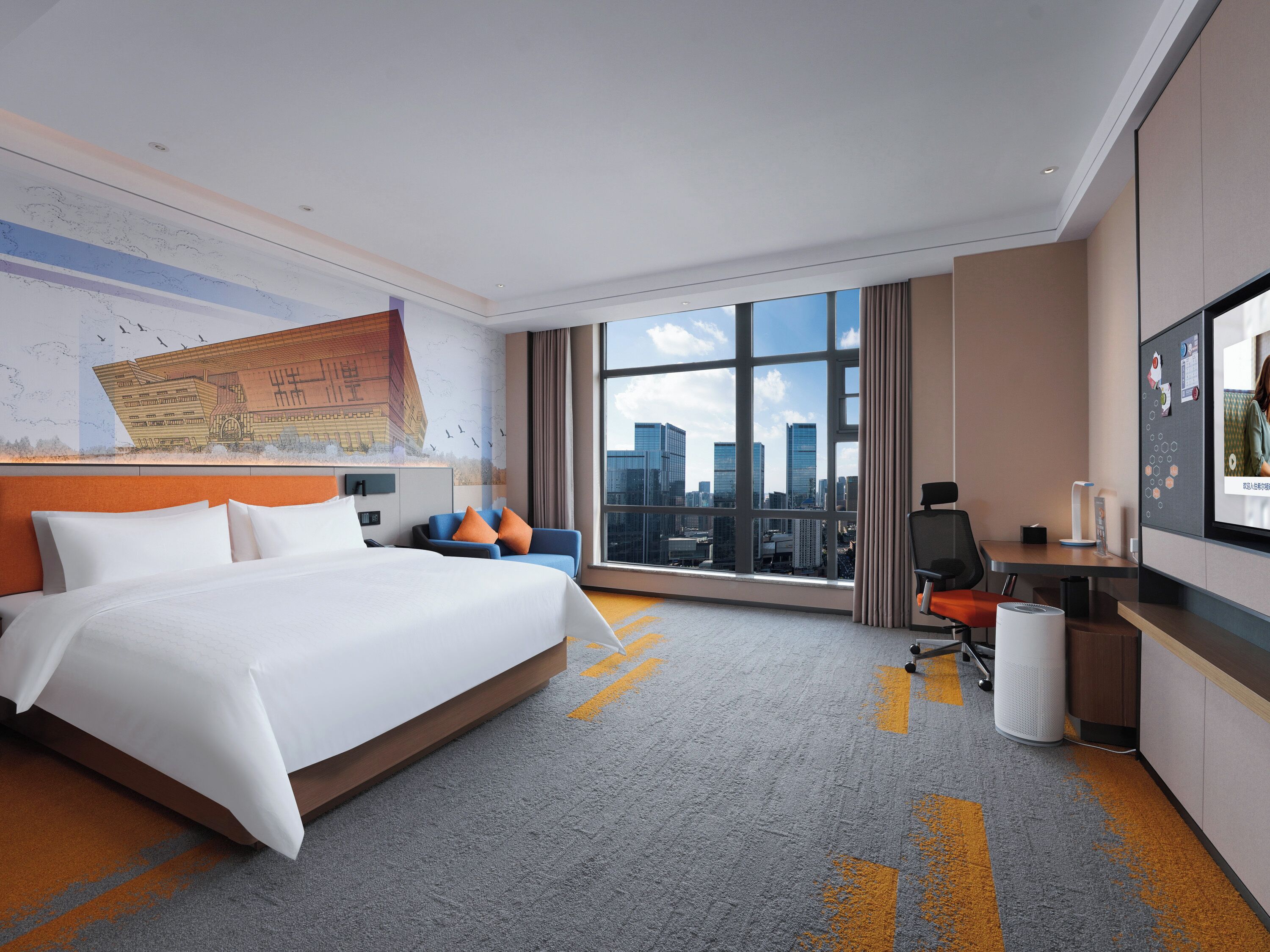 Ein Hotelzimmer mit einem großen Bett, einem Schreibtisch, einem Stuhl, einem Fernseher und Blick auf die Stadt.