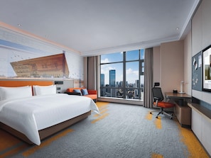 A hotel room with a large bed, a desk, a chair, and a city view.